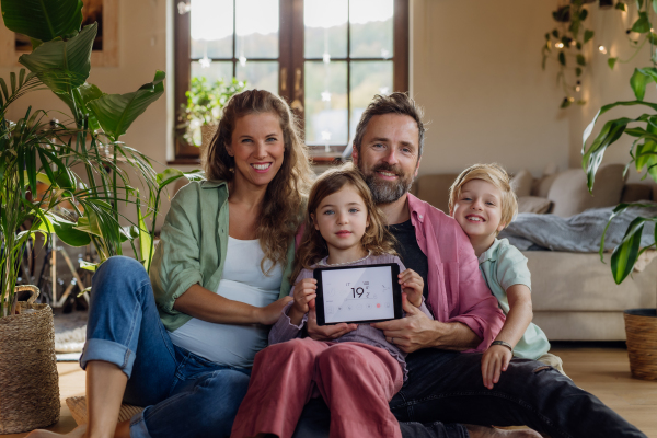 Family holding smart thermostat, adjusting or lowering heating temperatures at home. Concept of sustainable, efficient, and smart technology in home heating and thermostats.