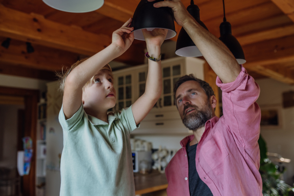 Father explaining led bubls to son, teaching him about energy efficiency, longevitiy and environmental impact. Son helping changing bulbs at home.