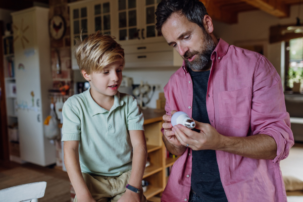 Father explaining led bubls to son, teaching him about energy efficiency, longevitiy and environmental impact. Son helping changing bulbs at home.