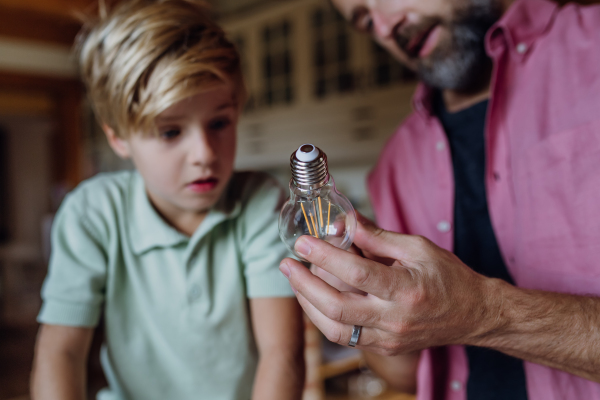 Father explaining led bubls to son, teaching him about energy efficiency, longevitiy and environmental impact. Son helping changing bulbs at home.