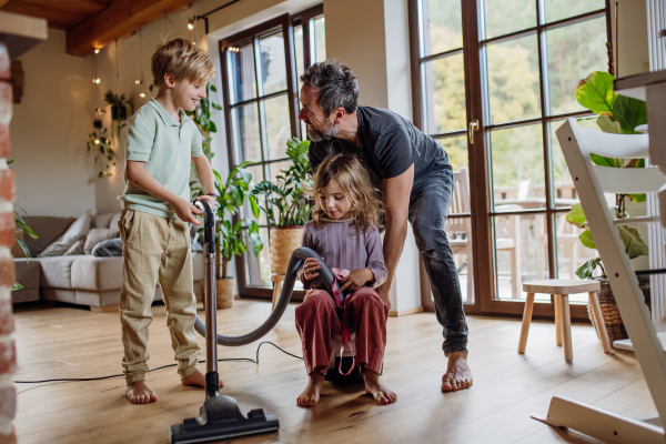 Father and kids cleaning house, vacuuming floors with a vacuum cleaner. Young boy and girl helping with house chores.