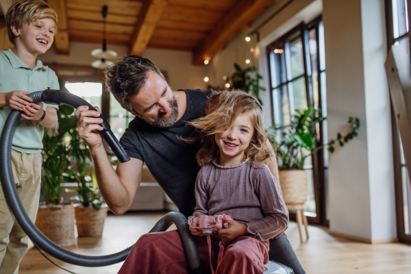 Father and son vacuuming girl's hair with vacuum cleaner. Father with kids cleaning the house, helping with house chores.