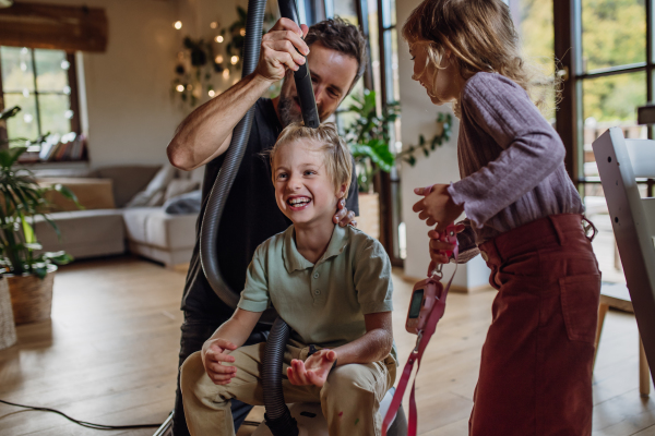 Father and vacuuming son's hair with vacuum cleaner. Father with kids cleaning the house, helping with house chores.