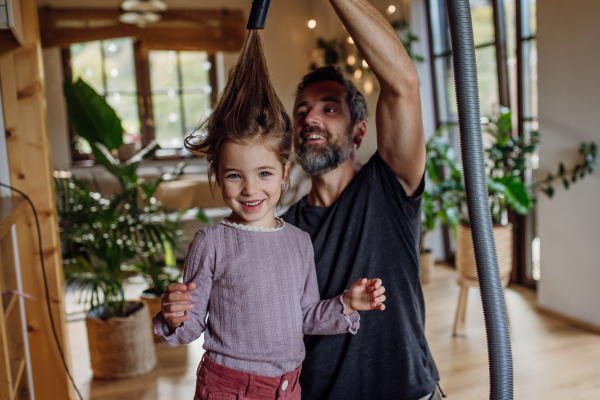 Father vacuuming girl's hair with a vacuum cleaner. Father and daughter cleaning the house, helping with house chores.