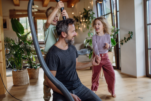 Father and kids cleaning house, vacuuming floors with a vacuum cleaner. Young boy and girl helping with house chores.