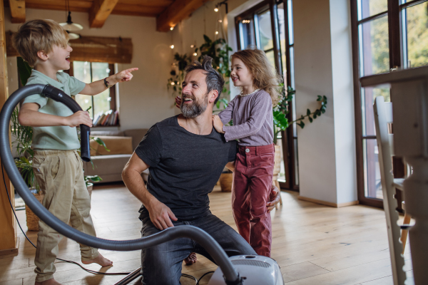 Father and kids cleaning house, vacuuming floors with a vacuum cleaner. Young boy and girl helping with house chores.