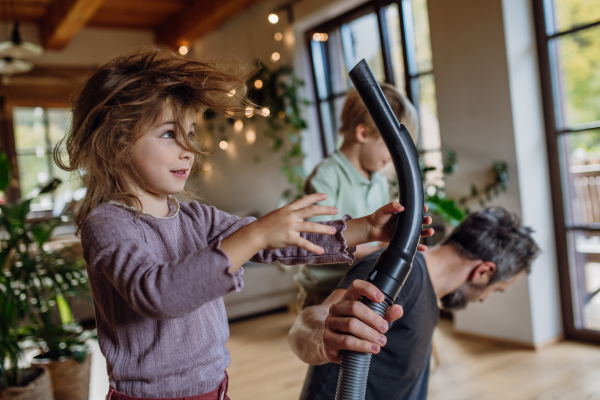 Father and son vacuuming girl's hair with vacuum cleaner. Father with kids cleaning the house, helping with house chores.