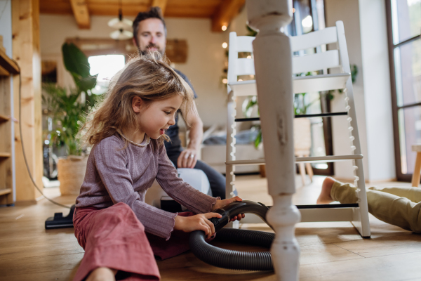 Young girl vacuuming the floors with a vacuum cleaner. Father and daughter cleaning the house, helping with house chores.