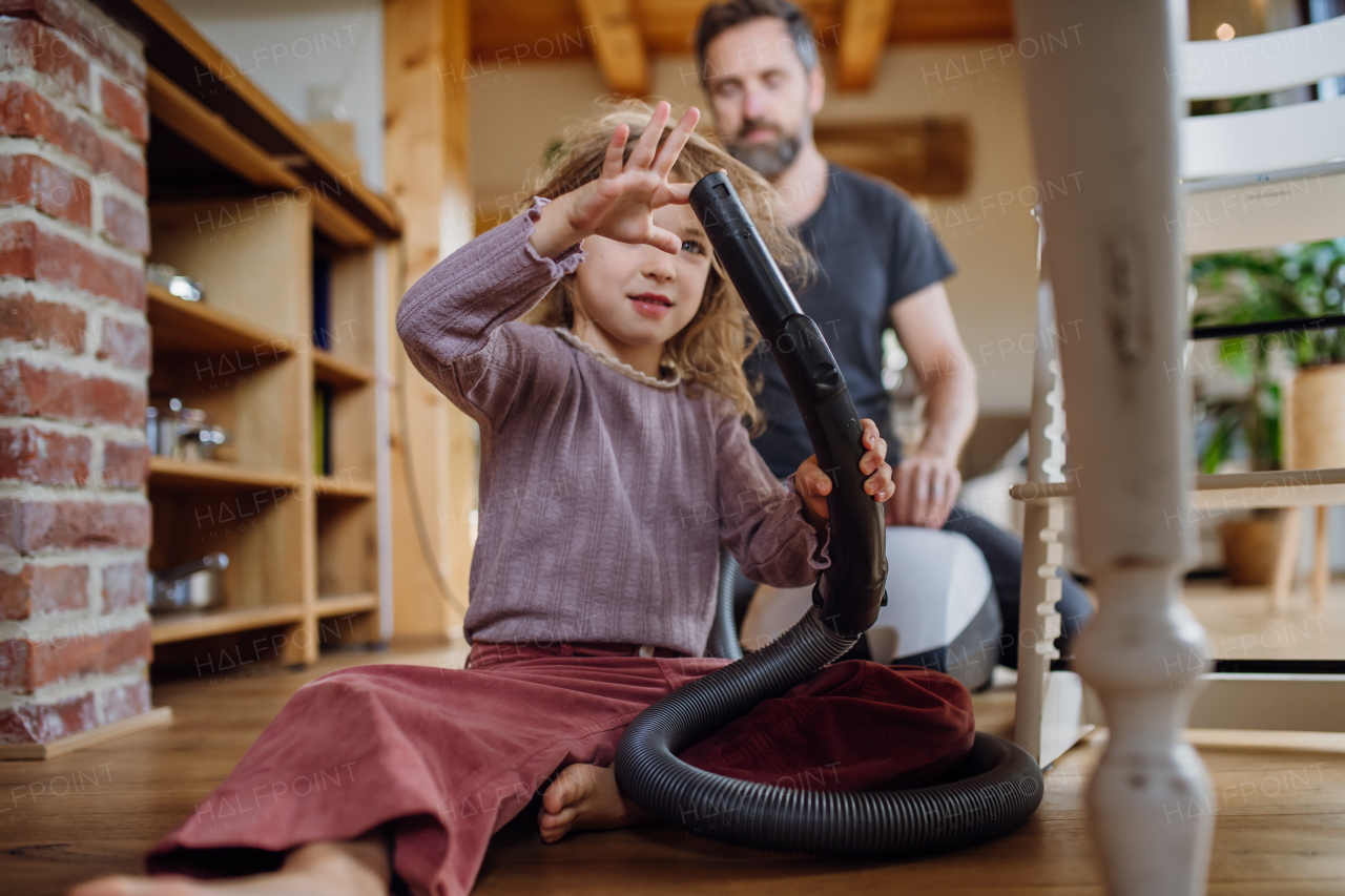 Father and daughter cleaning house, vacuuming floors with a vacuum cleaner. Young girl helping with house chores.