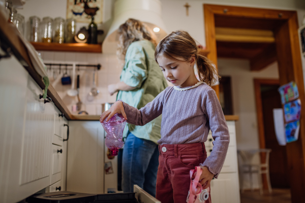 Girl throwing plastic bottles into recycling bin. Daughter sorting the waste according to material into colored bins in kitchen.