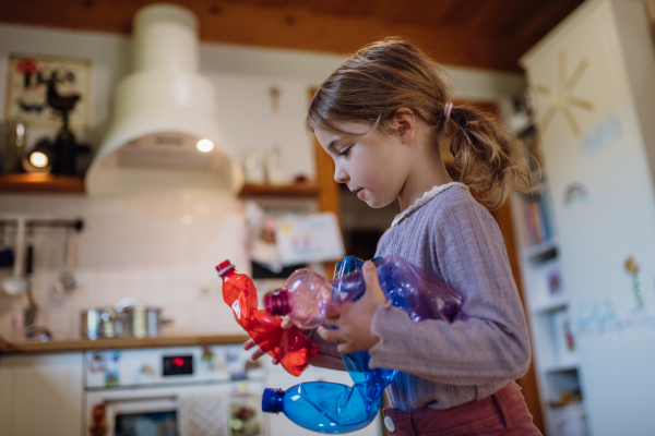 Girl throwing plastic bottles into recycling bin. Daughter sorting the waste according to material into colored bins in kitchen.