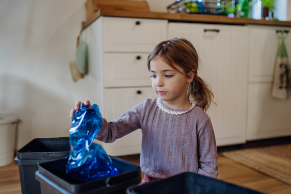 Girl throwing plastic bottles into recycling bin. Daughter sorting the waste according to material into kitchen bins.