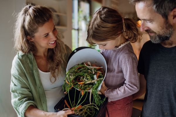 Girl helping parents to put kitchen waste, peel and leftover vegetables scraps into kitchen compostable waste. Concept of composting kitchen biodegradable waste.