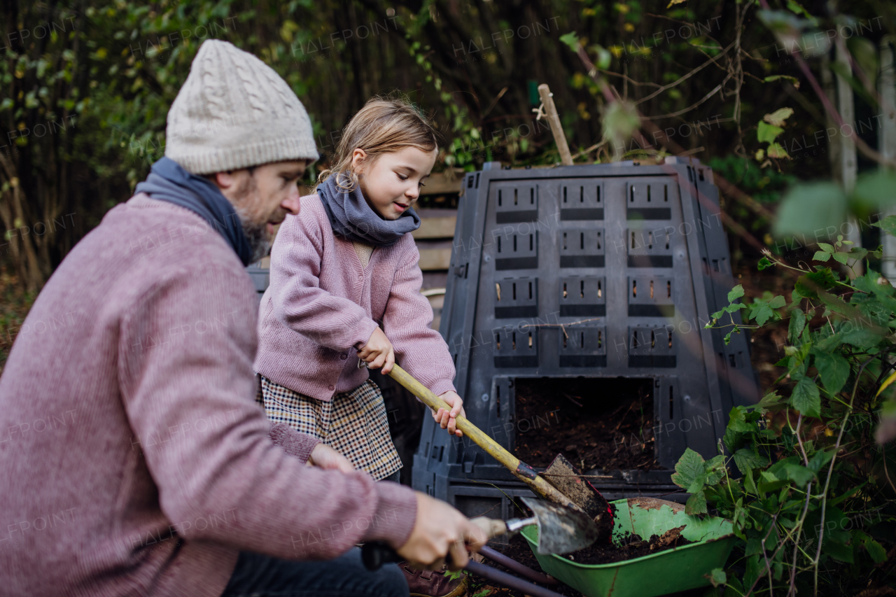 Girl helping father to remove compost from the composter in the garden. Concept of composting and sustainable organic gardening.