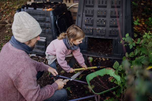 Girl helping father to remove compost from the composter in the garden. Concept of composting and sustainable organic gardening.