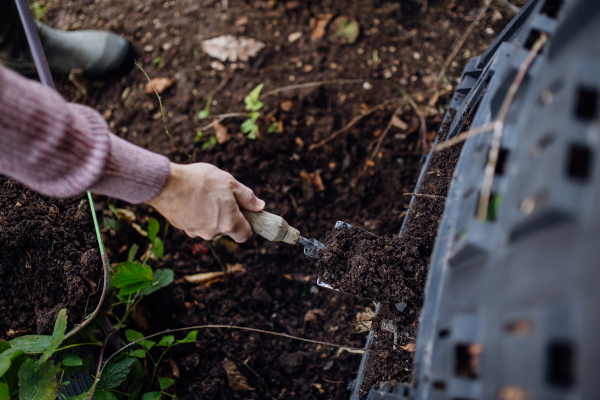 Girl removing compost from a composter in garden. Concept of composting and sustainable organic gardening.