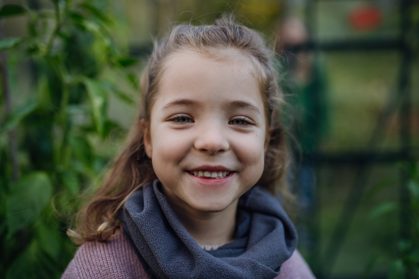 Portrait of little girl standing in greenhouse, during first spring days. Concept of water conservation in garden and family gardening.