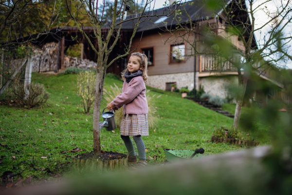 Little girl watering tree in the garden, using collected rainwater. Concept of water conservation in the garden and family gardening.