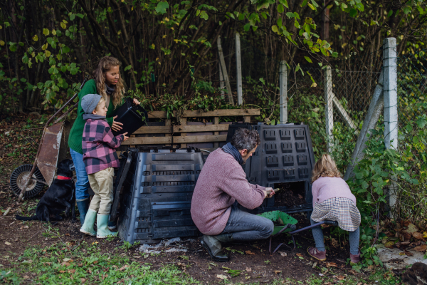 Family removing compost from a composter in garden, and also composting kitchen waste in composter. Concept of composting and sustainable organic gardening.