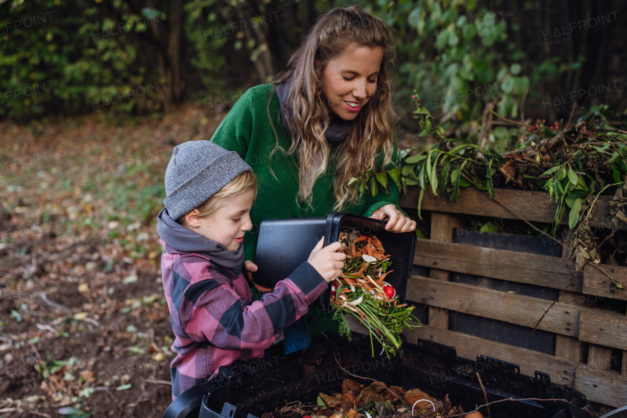 Boy helping mother to put kitchen waste, peel and leftover vegetables scraps into compostable waste, composter in the garden. Concept of composting kitchen biodegradable waste.