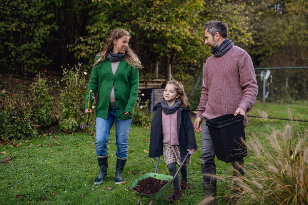 Front view of family taking care of home garden, planting tree. Mother, father and kids spending time outdoors during a cold autumn day.