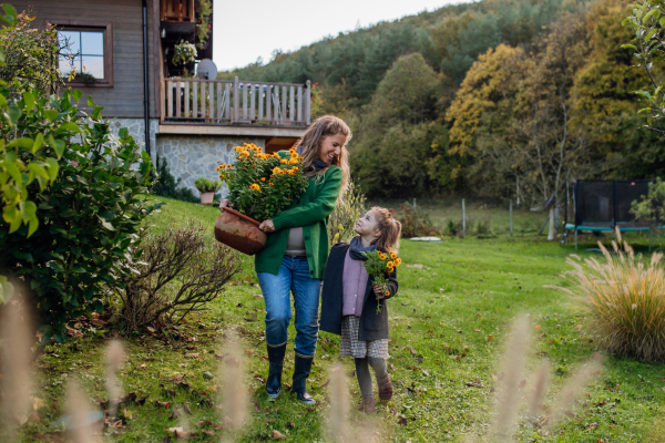 Mother and daughter taking care of home garden, replanting flowers. Pregnant mother spending time outdoors during a cold autumn day.