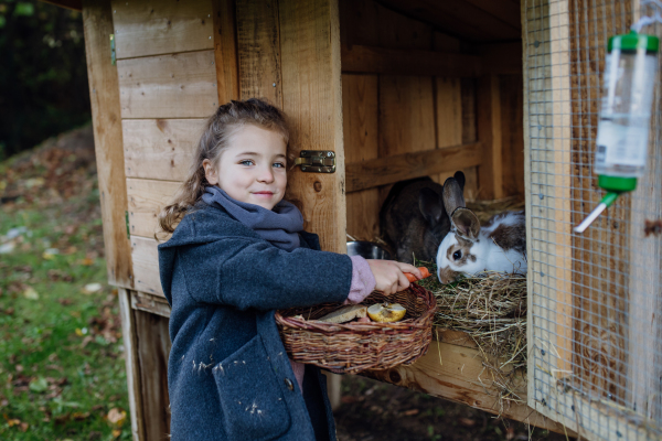 The girl is feeding the pet rabbit, giving it vegetables from the garden and old bread.