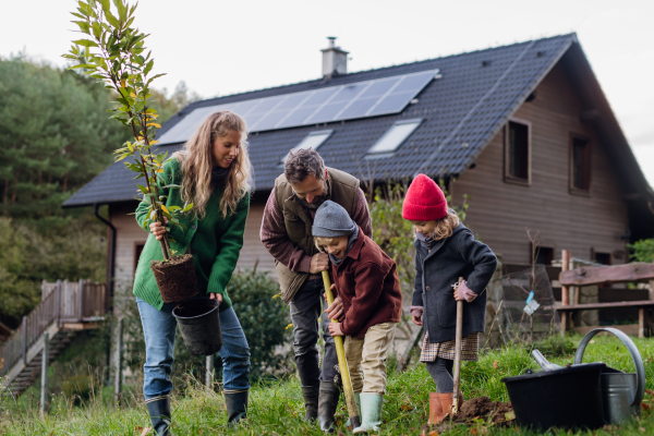 Front view of family taking care of home garden, planting tree. Mother, father and kids spending time outdoors during a cold autumn day.