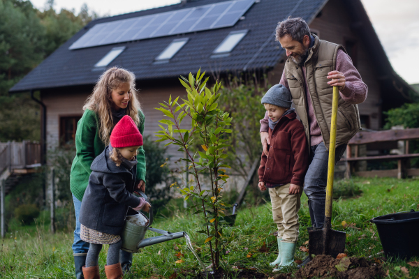 Front view of family taking care of home garden, planting tree. Mother, father and kids spending time outdoors during a cold spring, autumn day.