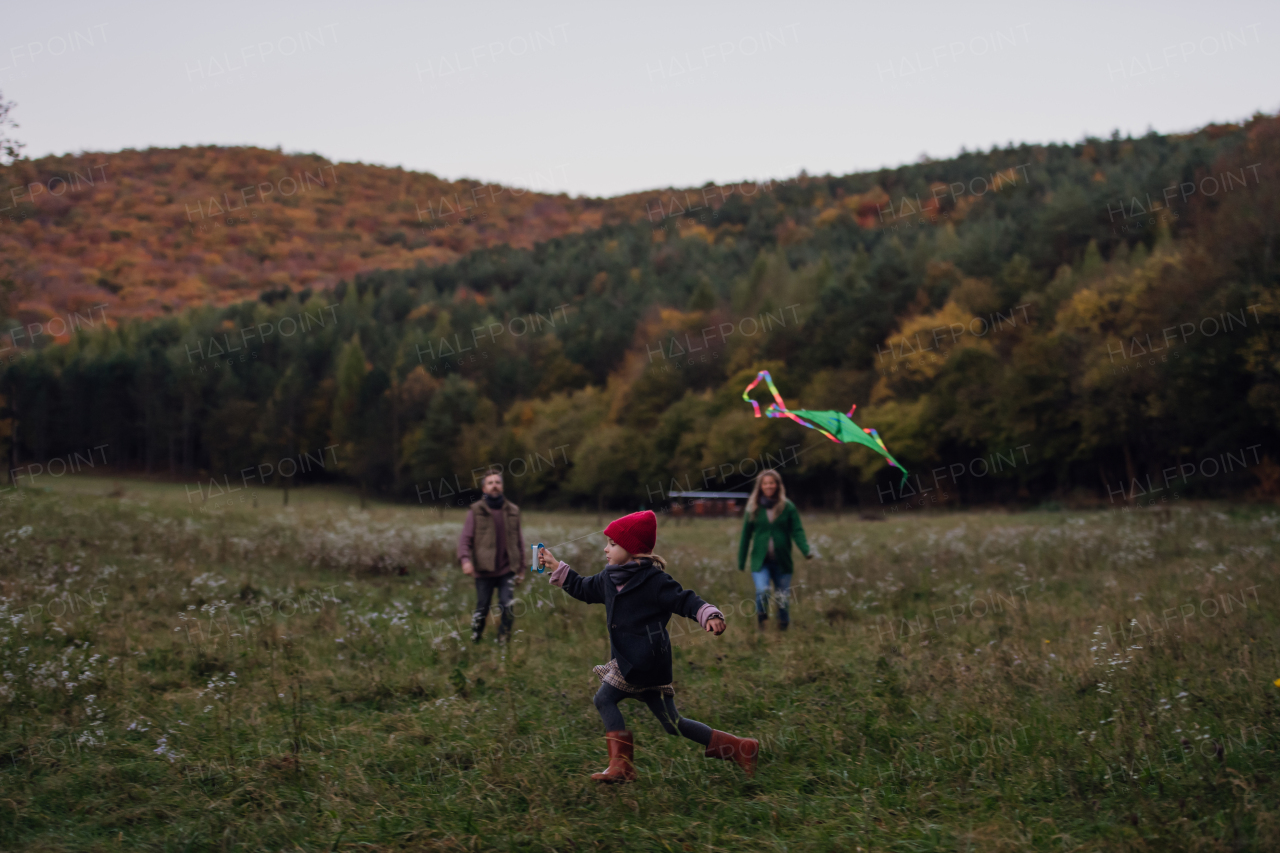 Girl flying a kite on meadow, running, having fun with parents. Autumn windy weather for kite flying.