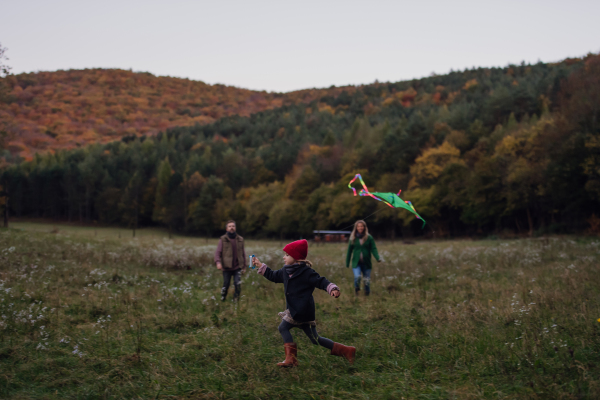 Girl flying a kite on meadow, running, having fun with parents. Autumn windy weather for kite flying.