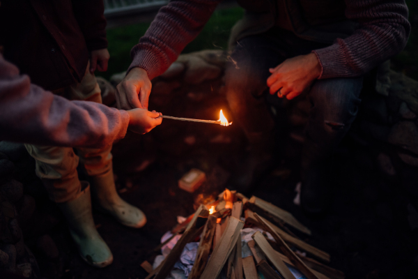 Family spending evening outdoors, lighting fire in a fire pit. Prents and kids spending quality family time together.