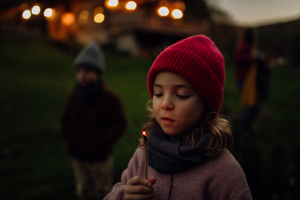 Portrait of a cute girl blowing out a flame on a burning stick. The family having a barbecue in the garden on an autumn evening.