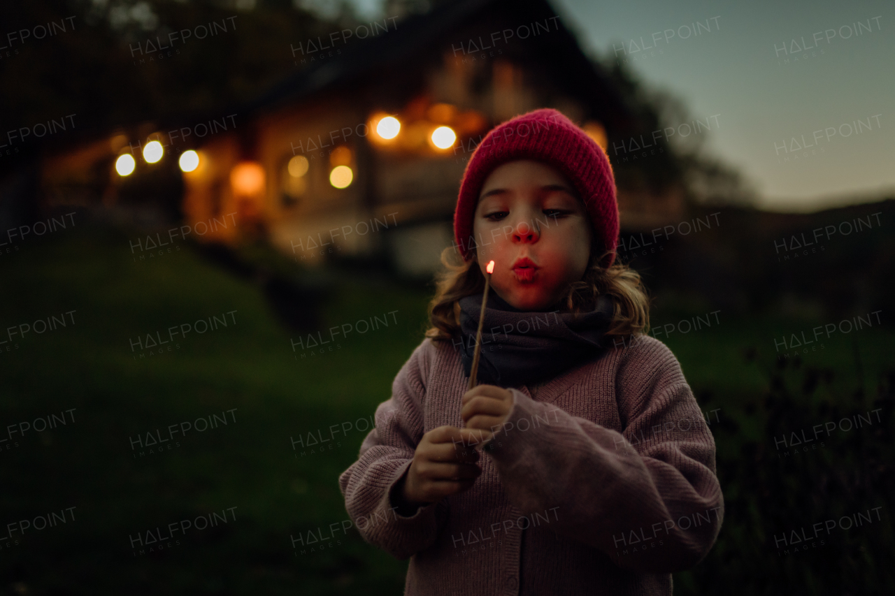 Portrait of a cute girl blowing out a flame on a burning stick. The family having a barbecue in the garden on an autumn evening.