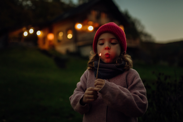 Portrait of a cute girl blowing out a flame on a burning stick. The family having a barbecue in the garden on an autumn evening.