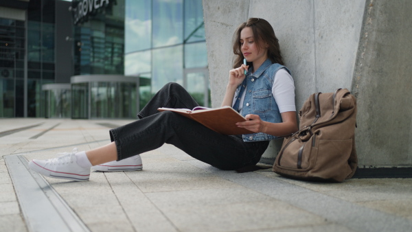 A video of focused beautiful student in front of university building or campus, studying outdoors, reading textbook, preparing for final exam.