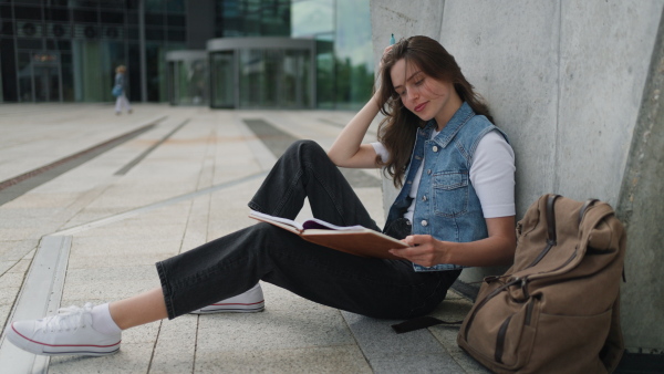 An university student sitting on ground in park, at campus and reading textbook. Studying before exam.