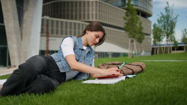 A video of female student lying on grass in front of university building or on campus. Studying outdoors, reading textbook, preparing for final exam.