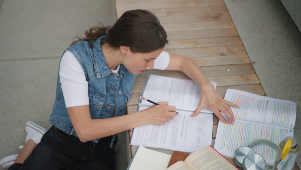 A video of focused beautiful student in front of university building or campus, studying outdoors, reading textbook, preparing for final exam.