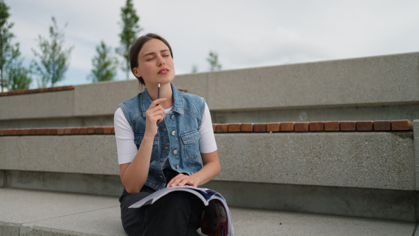 An university student sitting on ground in park, at campus and reading textbook. Studying before exam.