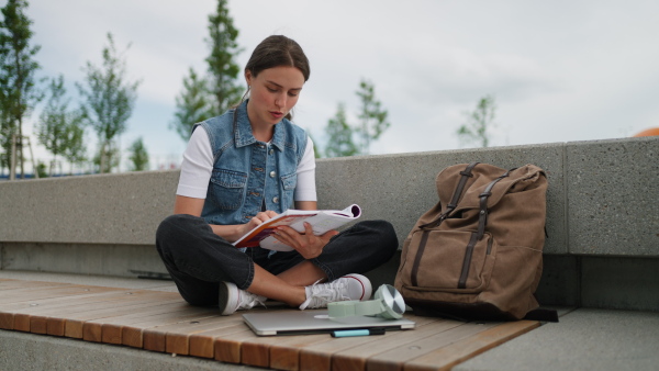 An university student sitting on ground in park, at campus and reading textbook. Studying before exam.