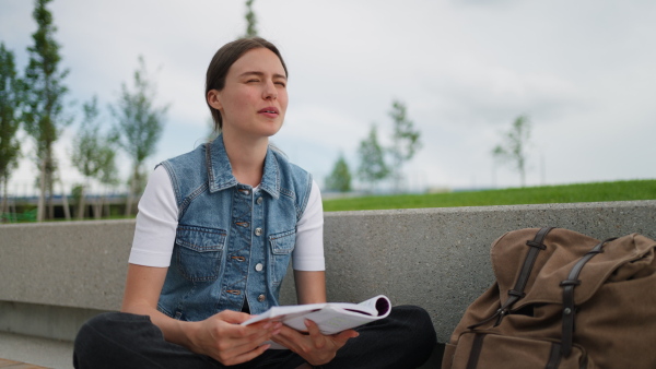 An university student sitting on ground in park, at campus and reading textbook. Studying before exam.