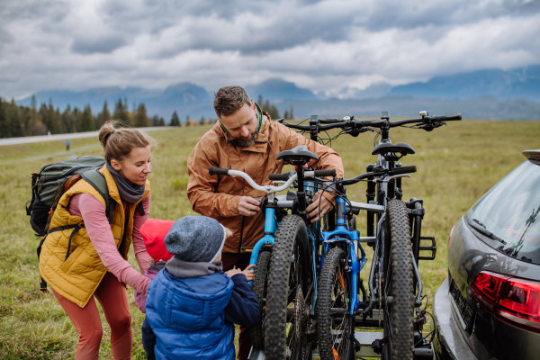 Young family with little children preparing for bicycle ride in nature, putting off bicycles from car racks. Concept of healthy lifestyle and moving activity.