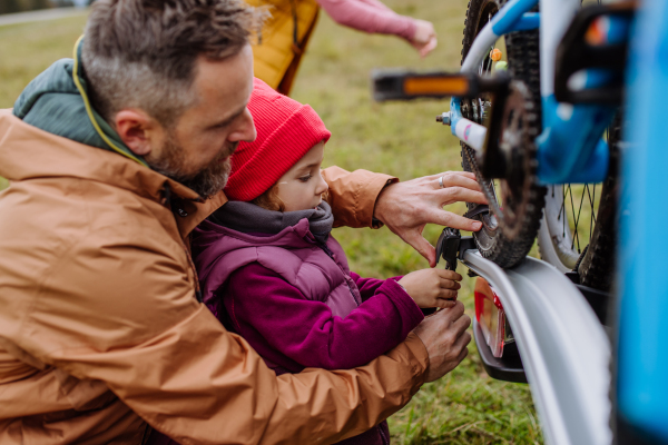 Littlle girl helping father attache a bicycle on bike carrier. Preparing for bicycle ride in nature, putting off bicycles from car racks. Concept of healthy lifestyle and moving activity.