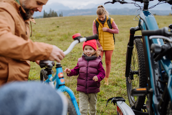 Young family with little children preparing for bicycle ride in nature, putting off bicycles from car racks. Concept of healthy lifestyle and moving activity.