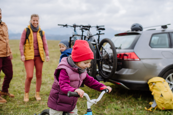 Young family with little children preparing for bicycle ride in nature, putting off bicycles from car racks. Concept of healthy lifestyle and moving activity.