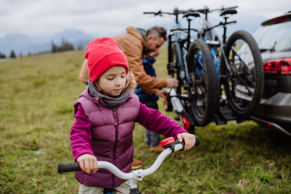 Young girl looking forward to bicycle ride in nature. Father putting off bicycles from car racks. Concept of healthy lifestyle and moving activity.