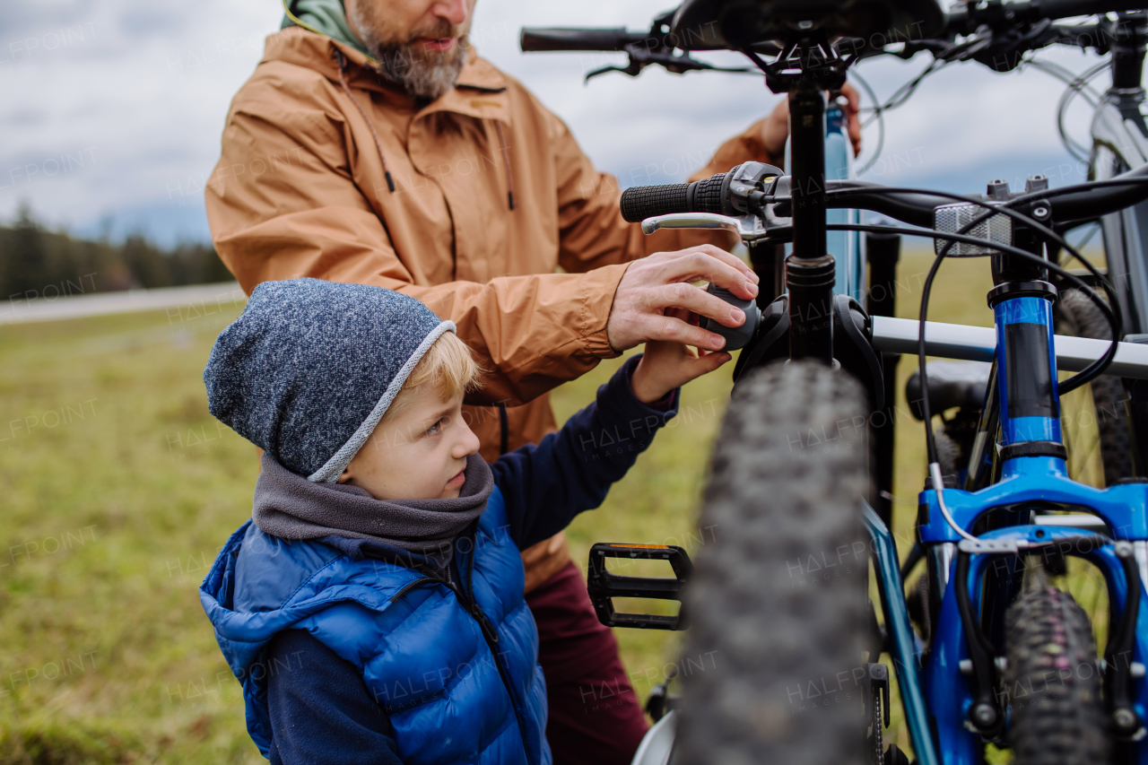 Young family with little children preparing for bicycle ride in nature, putting off bicycles from car racks. Concept of healthy lifestyle and moving activity.