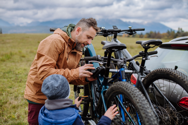 Littlle boy helping father attache a bicycle on bike carrier. Preparing for bicycle ride in nature, putting off bicycles from car racks. Concept of healthy lifestyle and moving activity.