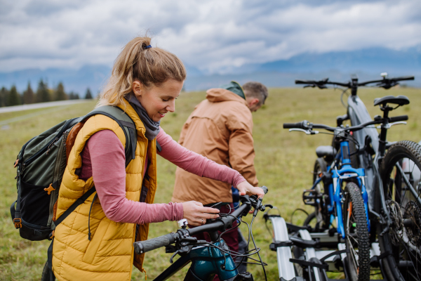 Young family preparing for bicycle ride in nature, putting off bicycles from car racks. Concept of healthy lifestyle and moving activity.